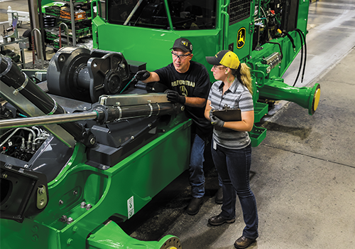 Female & Male employees at John Deere Inspecting a machine.
