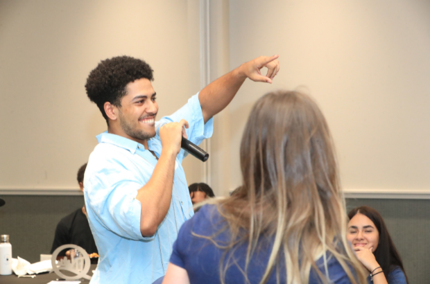 Smiling Man pointing while we speaks into a microphone
